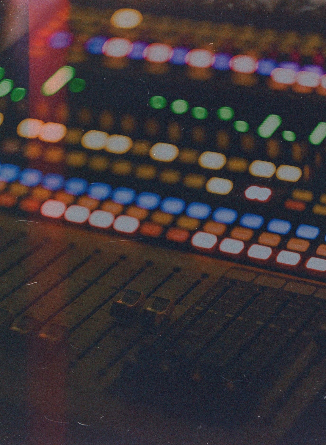 Backlit pads and faders of a mixing console glowing in the dark.
